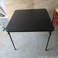 Top view of square black padded card table surface with small scuffs visible.