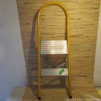 Front view of vintage yellow folding stepladder with two aluminum steps and curved top handle.