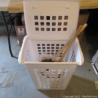 White plastic laundry basket with lid open showing contents inside on a concrete floor.