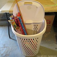 Front view of white plastic laundry basket filled with rolls of wrapping paper and other miscellaneous items