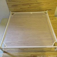 Full view of the laundry drying sheet frame showing white tubular metal frame and mesh surface on a wood patterned floor.