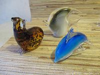 Three decorative glass animals: amber owl, gray stingray, blue dolphin