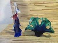 Both glass ornaments side by side on neutral surface with wood slat backdrop