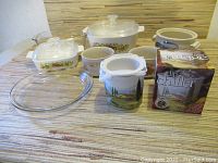 Wide shot of all dishes and dip chiller on a beige textured tablecloth, showing covered casserole dishes, glass bakeware, ceramic mug, and dip chiller with box.