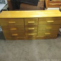 Front view of the oak chest of drawers showing three columns of three drawers each with oak handles, placed on carpeted floor.