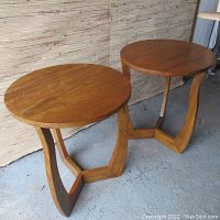 Both round-top fruitwood side tables shown side by side on concrete floor against wood panel backdrop