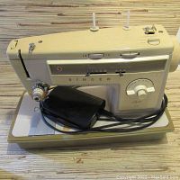Side angle of vintage cream-colored Singer sewing machine with foot pedal and cord, showing stitch options and dials