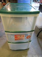 Front view of the plastic storage shelf showing three transparent drawers with green trim and green top panel.