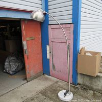 Tall full view of the metal floor lamp showing curved stem and marble base outside a building.