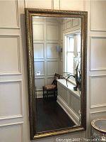 Front view of full-length mirror leaning against paneled wall