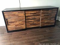 Front view showing black top and sides with multi-tone wood front panels, three drawers centered, sliding doors on each side