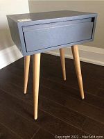 Contemporary lamp table showing drawer and natural wood legs, viewed side angle