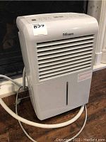 Front and top view of white Danby Premiere dehumidifier showing front air vents, water collection tank, control buttons on top, and white drainage hose coiled around the base.