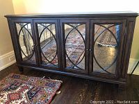 Front view of dark brown buffet cabinet with four mirrored doors and circular wood overlay, patterned rug beneath.