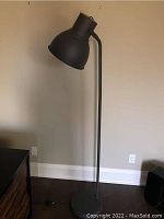 Full standing view of the matte black contemporary floor lamp against a beige wall showing round flat base and tall slim pole.
