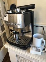 Front view of Krups espresso machine showing buttons, portafilter, metal frothing pitcher, white ceramic mug and warming coaster adapter
