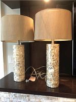 Two cylindrical mother of pearl mosaic table lamps with beige drum shades and cords visible