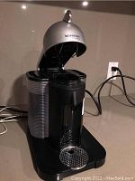 Front view of Nespresso VertuoLine coffee machine showing water reservoir, drip tray and power cord.