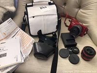 Camera body, two lenses, bag, manuals and charger arranged on sofa