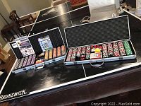 Two open poker chip cases sitting on a ping pong table showing poker chips, playing cards and buttons