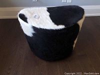 Side view of the black and white cowhide ottoman showcasing its texture and shape.
