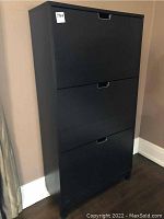 Front view of the closed black shoe storage cabinet with three compartments and cutout handles.