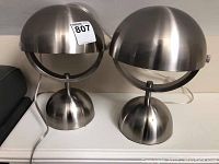 Pair of brushed stainless steel contemporary table lamps with dome-shaped shades and weighted round bases, size approximately 12 inches high.