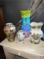 Front view photo showing four ceramic vases with various floral and color patterns, displaying varying heights and designs