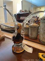 Full view of the crystal glass bird statue on a wooden surface with other decorative items in background.