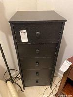 Front view of black five drawer wooden cabinet showing vertical drawers with round knobs and surface scratches.