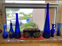 View of all items lined up on windowsill showing variety of blue glass vases and painted nautical flower pot