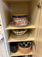 Cabinet shelf with colorful ceramic mixing bowl, smaller bowl, and matching platter with floral and geometric patterns