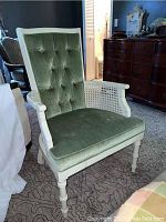 Front angled view of a green tufted fabric chair with white painted wood frame and rattan sides.