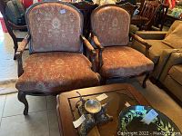Two Bernhardt dark accent chairs side by side with a glass topped wooden table in front, showing fabric upholstery and wooden frames with armrests and legs.