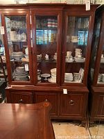Front view of dark wood china cabinet with glass doors showing dishes inside and wood bottom storage with doors.