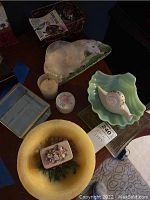 Photo showing multiple collectibles including a yellow bowl, a ceramic snail-shaped dish, small candles, and a floral pill box inside the bowl.