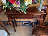 Front view of the wood console table showing the polished surface, center drawer with metal handles, and curved legs.