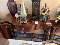 Full view of Maitland-Smith console table with curved edges, three front drawers, and carved legs topped with various decorative items.
