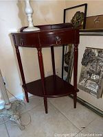 Front angled view of dark wood corner table showing drawer with ring pull hardware, turned legs, and lower shelf.