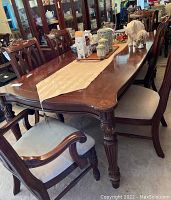 View showing six dark wood dining chairs around a long dining table, two with armrests, light fabric seats, and carved decorative backs and legs.