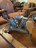 Front angled view showing three brass elephants with raised trunks and center bowl on a decorative base.
