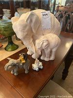 Large white elephant and calf statue with intricate floral texture details on the surface, positioned behind three smaller figurines on a wooden table.
