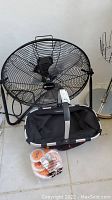 Utilitech floor fan with three blades and black frame, Reisenthel fabric basket, small orange tape rolls in front on the floor