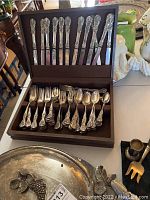 Wooden hinged presentation case open showing twelve floral-handled knives secured in lid slots