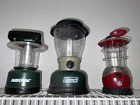 Image showing three lanterns from front: Rayovac green lantern, Coleman large lantern with frosted globe, and red GE lantern.