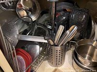 Various kitchen items on a metal rack including lids, bowls, cutlery holder with utensils, slotted spatula, and bakeware pieces.