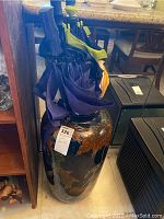 Photo of large floor vase holding ten umbrellas, showing decorative pattern and multiple umbrella handles