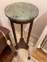 Full view of round light green marble top with wood pedestal base featuring three legs and tiled floor background.