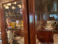 Wooden cabinet shelves with stacked yellow pottery and dishes, Asian-inspired containers, glassware, and assorted ceramic items