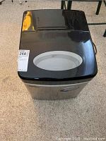 Front view of electric ice maker showing black lid with oval transparent window.